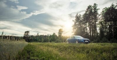 white car on green grass field near green trees under white clouds during daytime